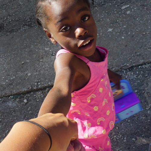 A little girl in pink is holding onto someone 's hand